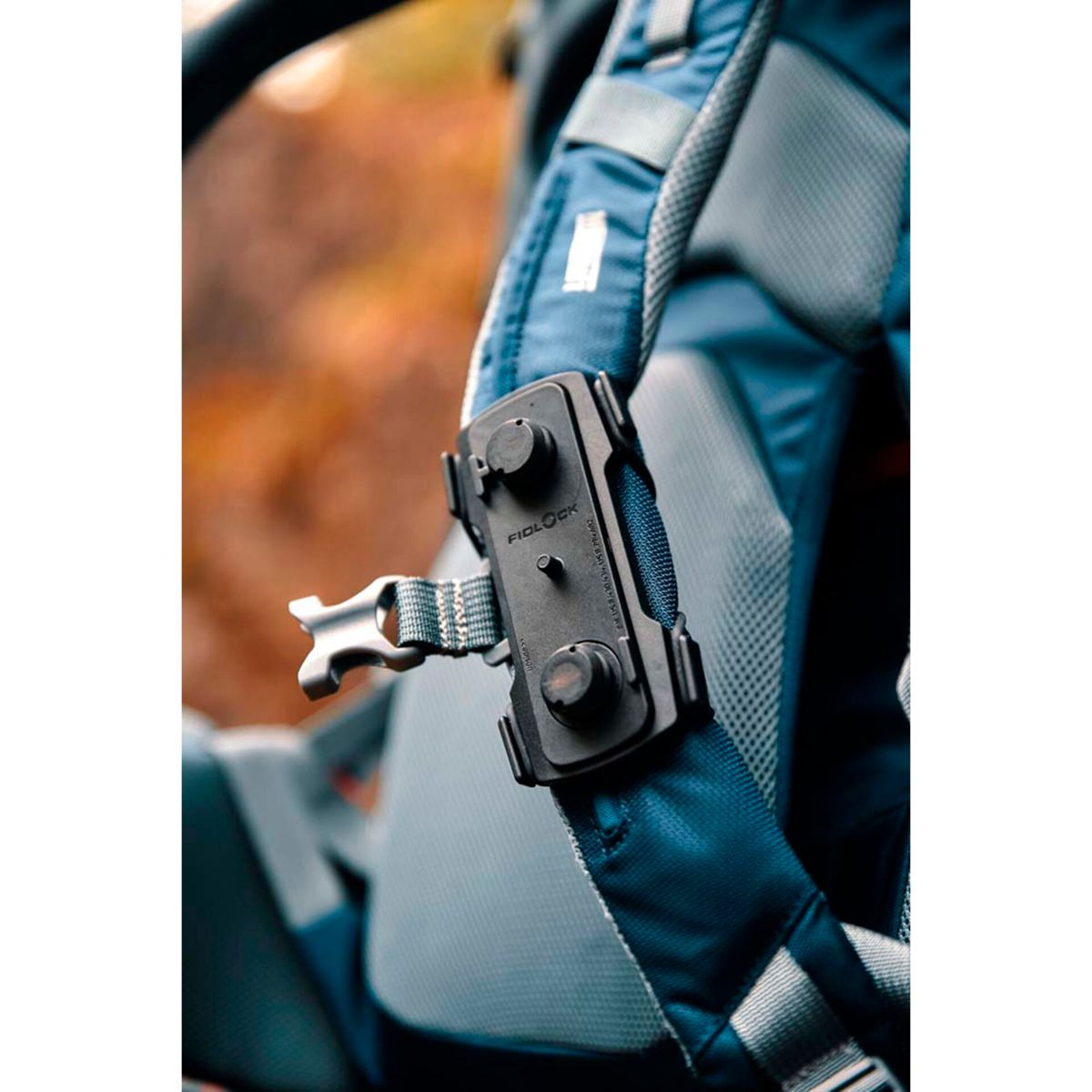 Eine schwarze magnetische Fidlock-Halterung ist am blauen Rucksackriemen befestigt.