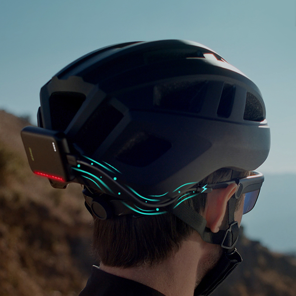 Schwarzer Fahrradhelm mit rotem Rücklicht und blauen Lichtern, im Freien getragen.