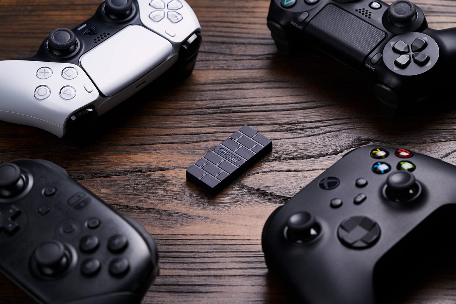 Vier Videospiel-Controller und ein schwarzer Adapter sind auf einer Holzoberfläche angeordnet.