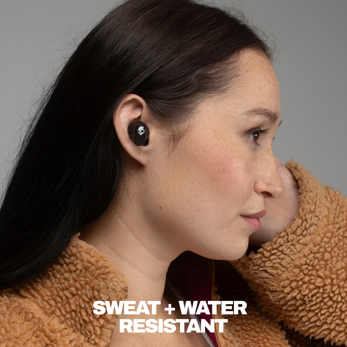 Frau mit schwarzem Ohrhörer, der ein Totenkopf-Logo trägt. Sweat + Wasserbeständig.