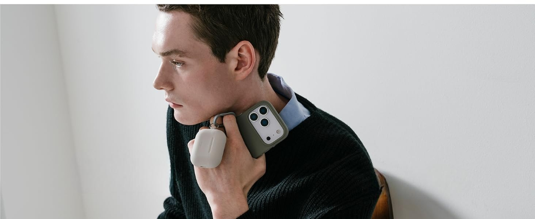 Mężczyzna w ciemnym swetrze i niebieskiej koszuli trzyma telefon i etui ładujące.