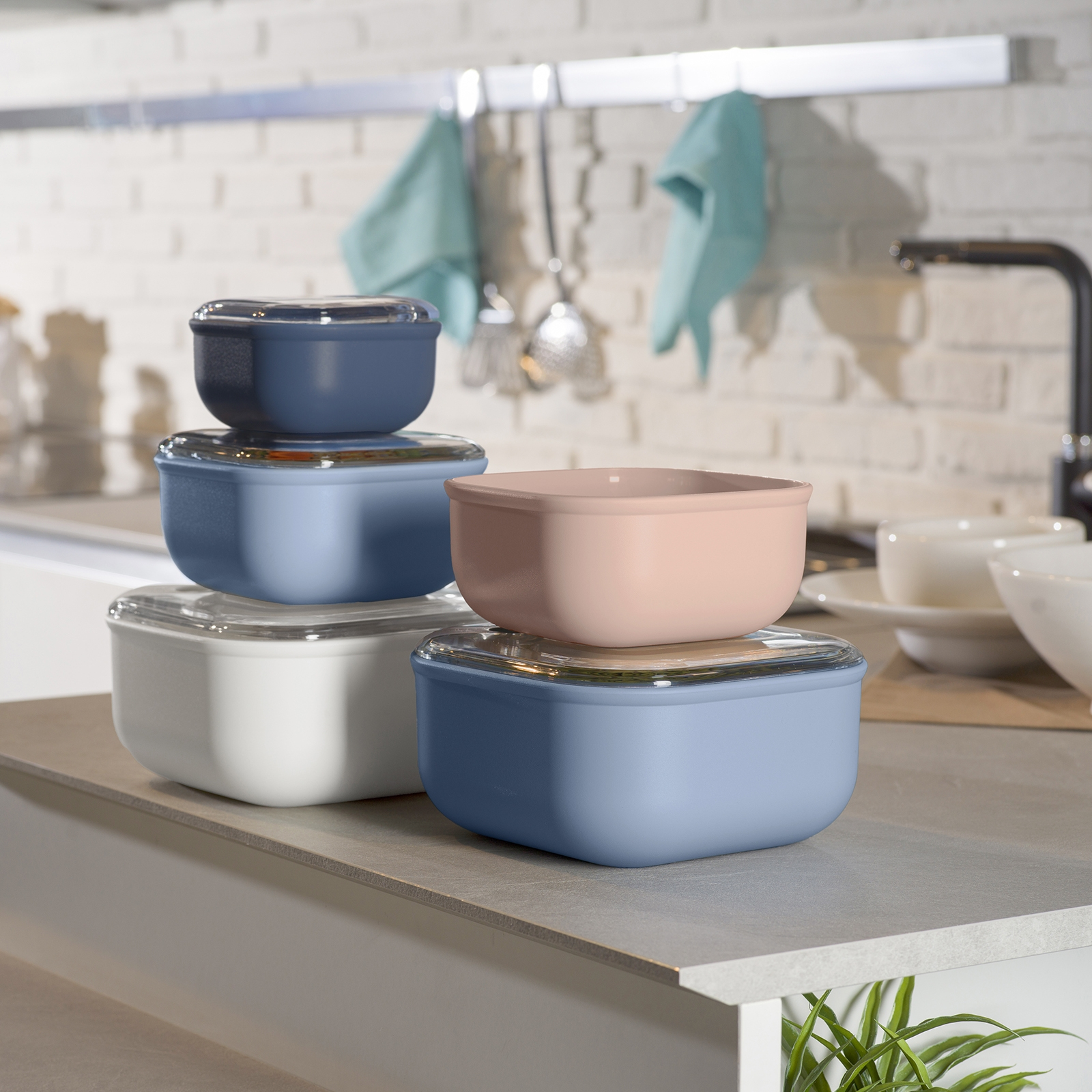 Diversi contenitori colorati per alimenti con coperchi sono impilati in cucina.
