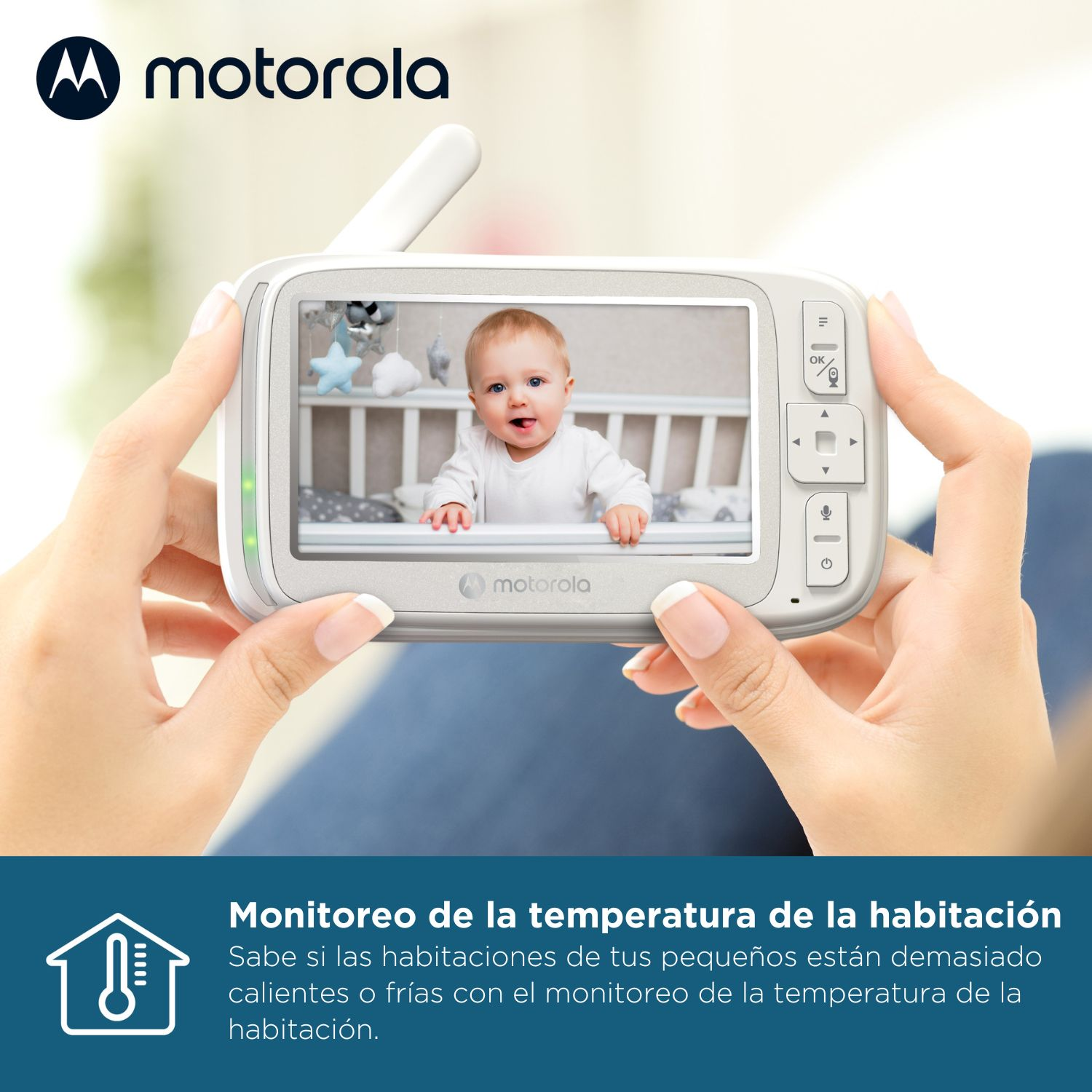 Una mano tiene un baby monitor con un bambino sorridente in una culla sullo schermo.