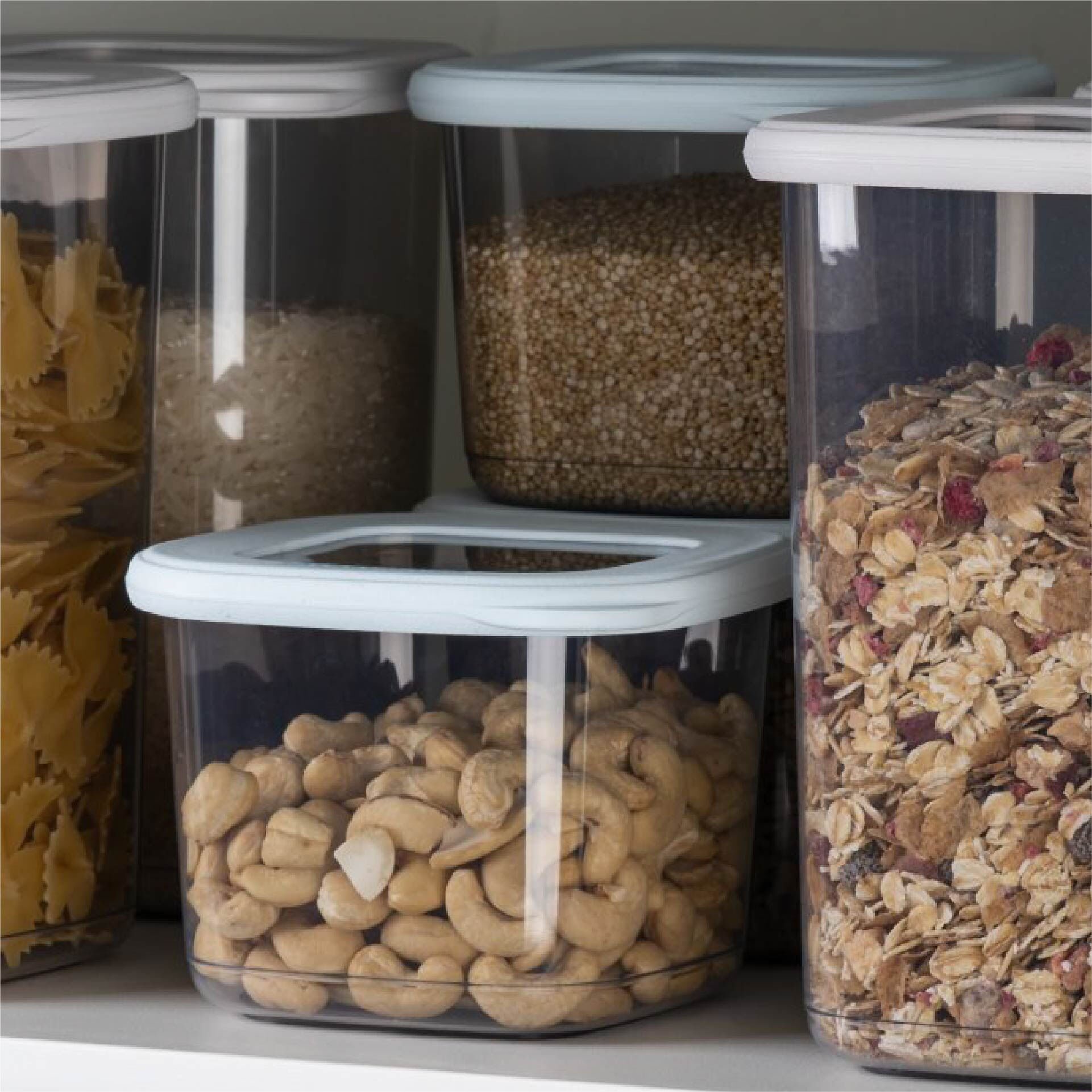Plusieurs récipients alimentaires transparents remplis de pâtes, riz, noix et céréales.
