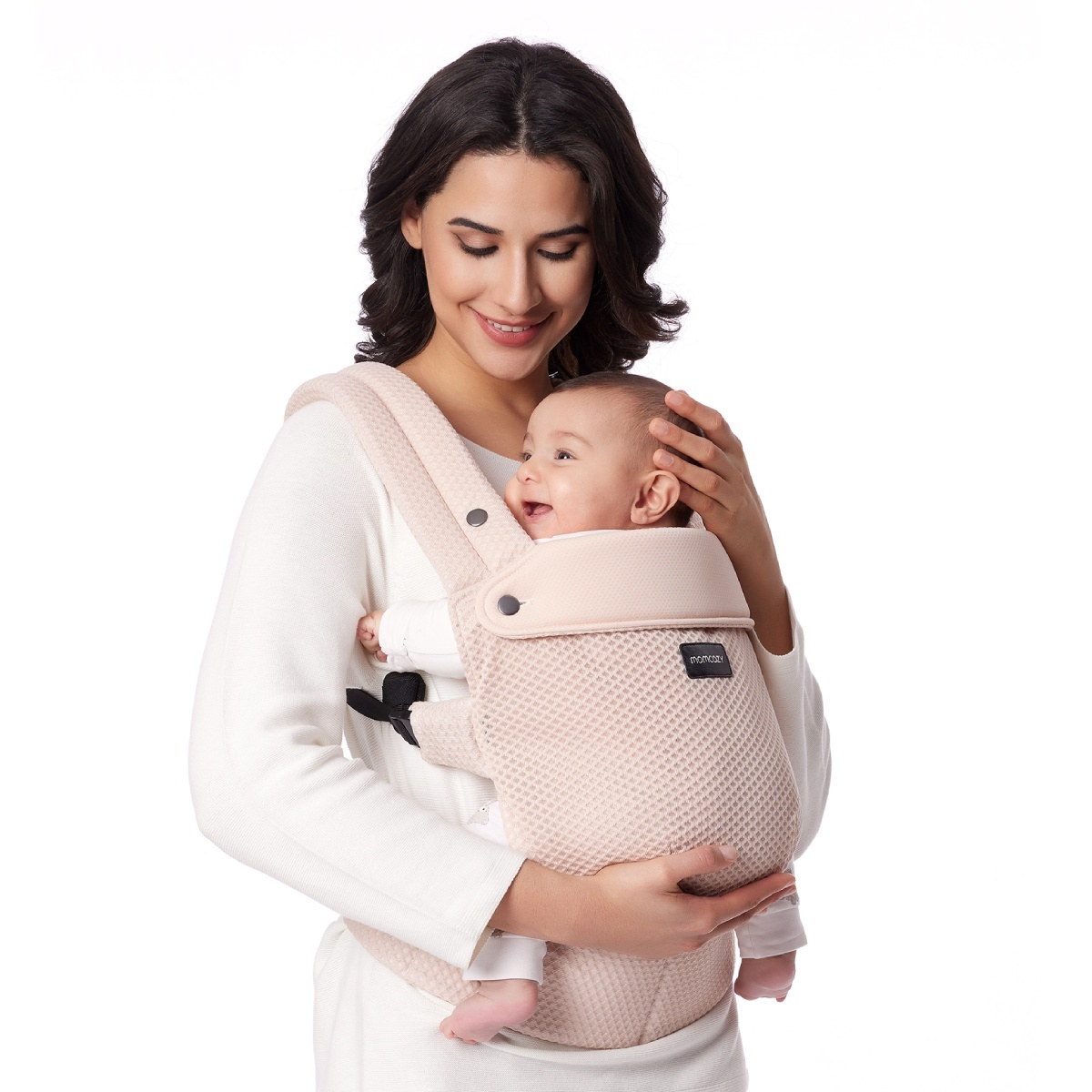 Eine Frau trägt ein Baby in einer rosa Trage. Beide lächeln.
