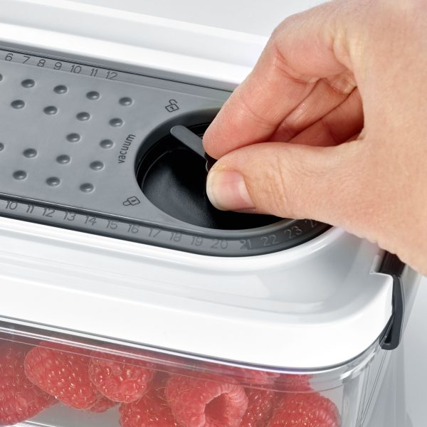 Hand dreht an einem Drehknopf auf einem Behälter mit Himbeeren.