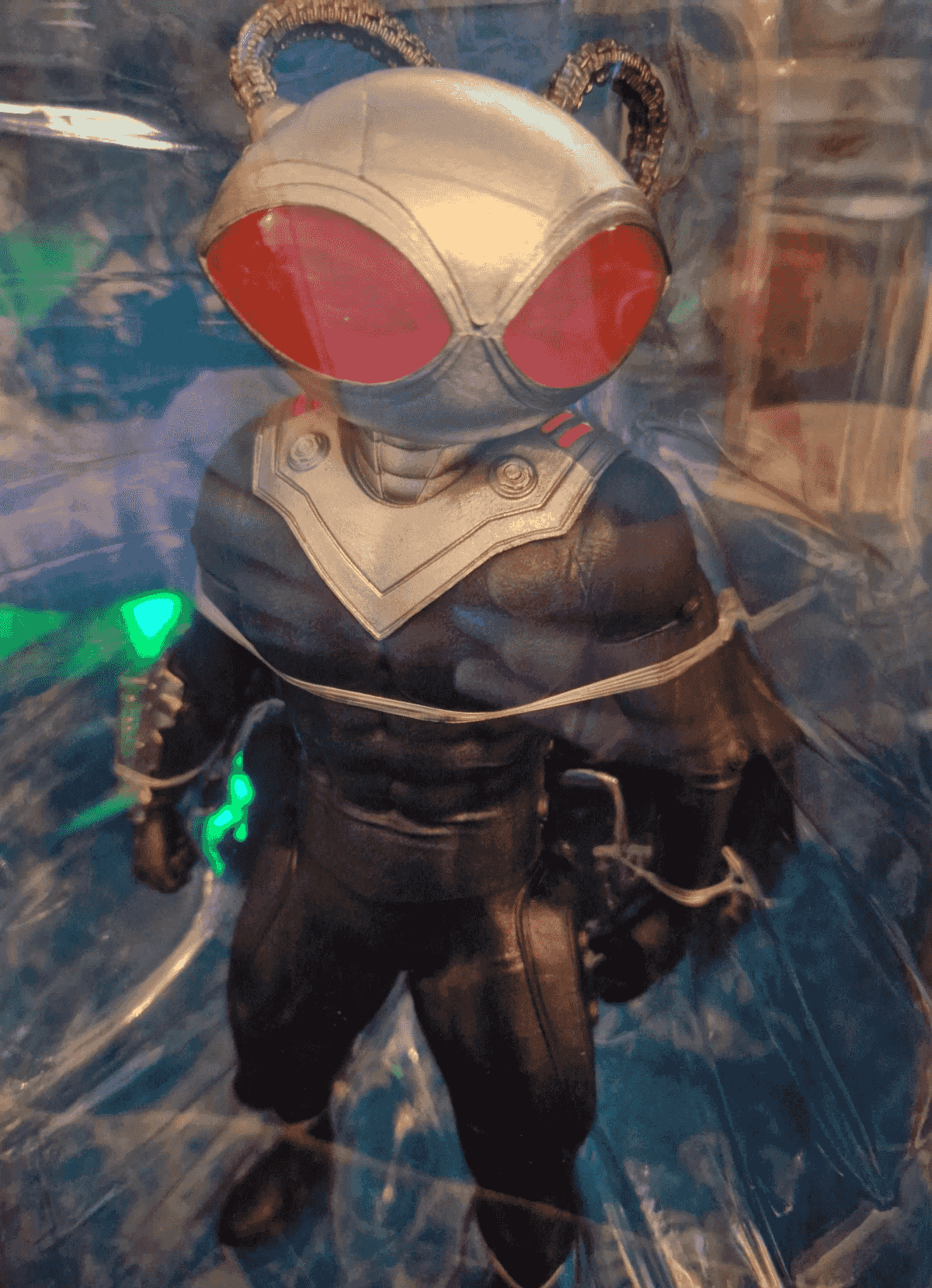 Una figura de acción de Black Manta con casco plateado, ojos rojos y traje negro.