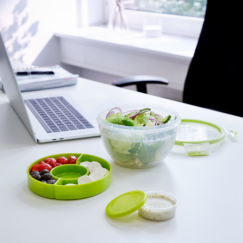 Büro-Schreibtisch mit Laptop, Salat und Snackschale.