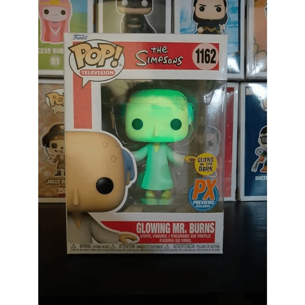 Figura Funko Pop! de Mr. Burns brillante en caja, con otros juguetes al fondo.