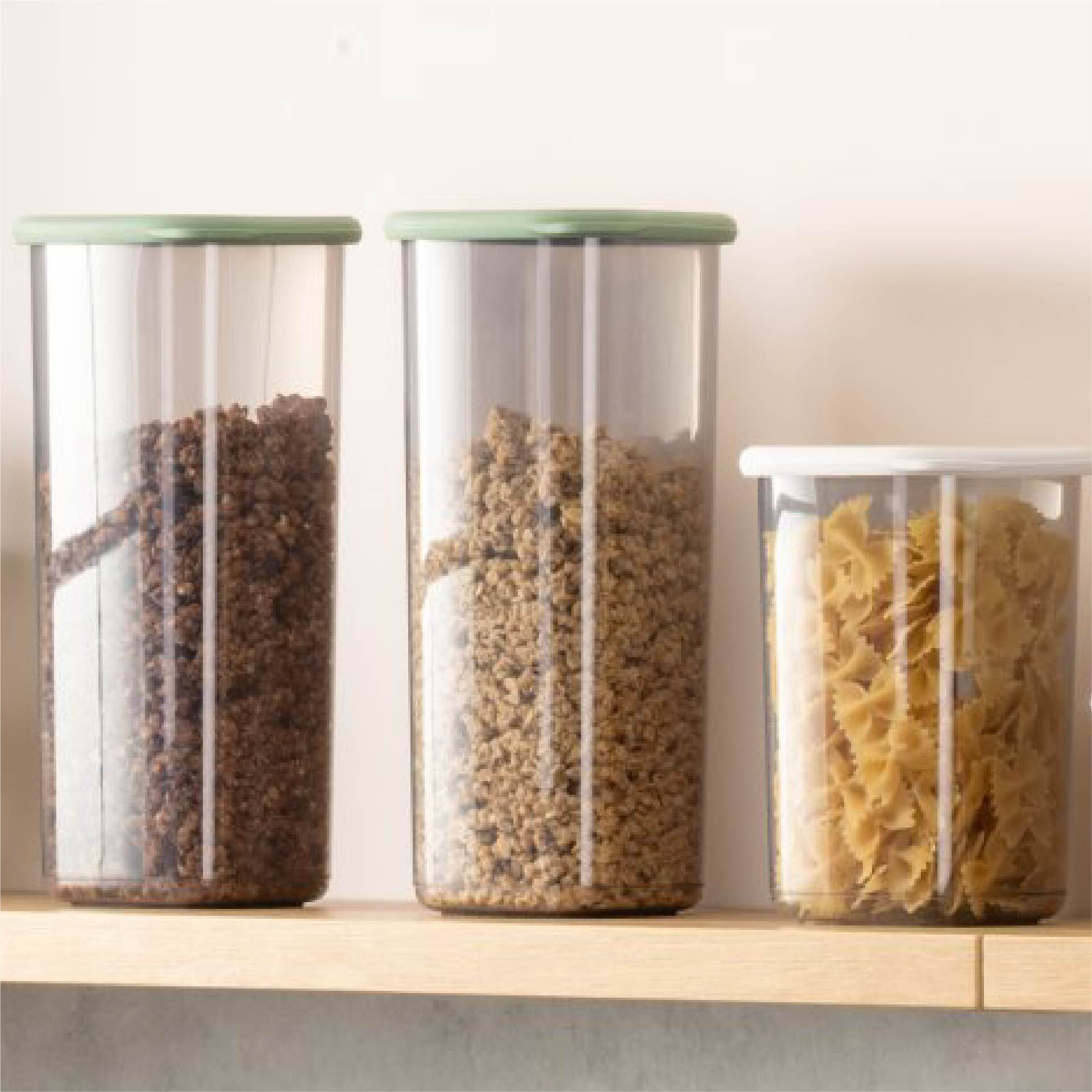 Tre contenitori trasparenti per alimenti, due con granuli marroni, uno con pasta.