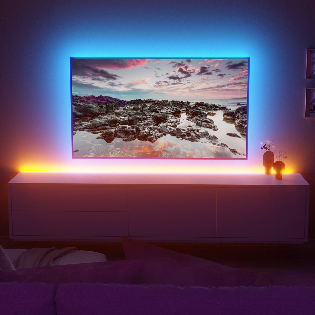 Una TV mostra una costa rocciosa con cielo drammatico, incorniciata da luci ambientali blu e gialle.