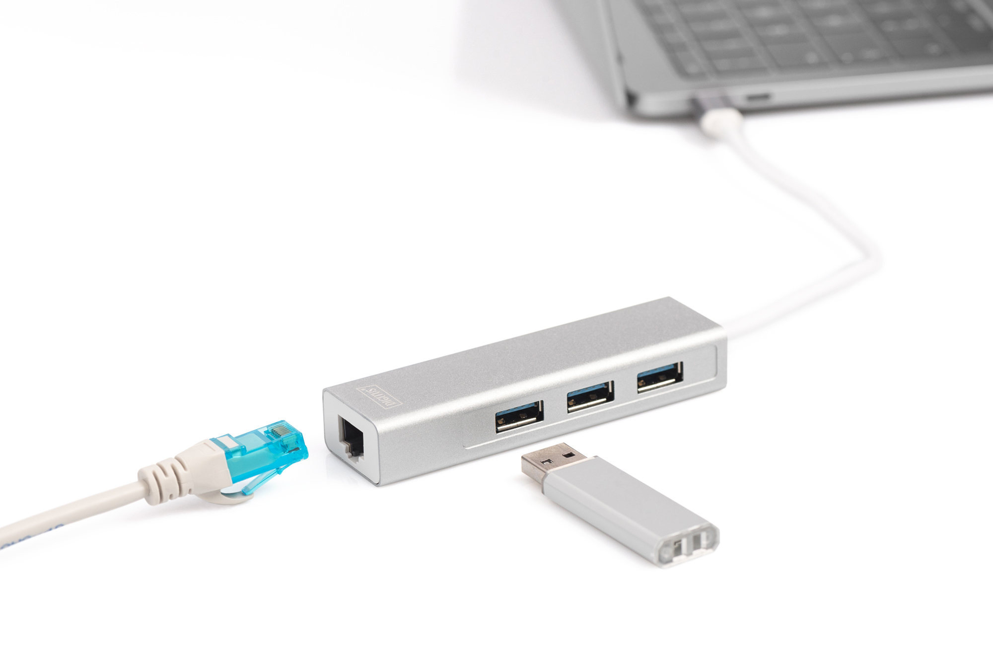 Zilveren USB-hub met drie poorten, Ethernet en USB-stick naast een laptop.