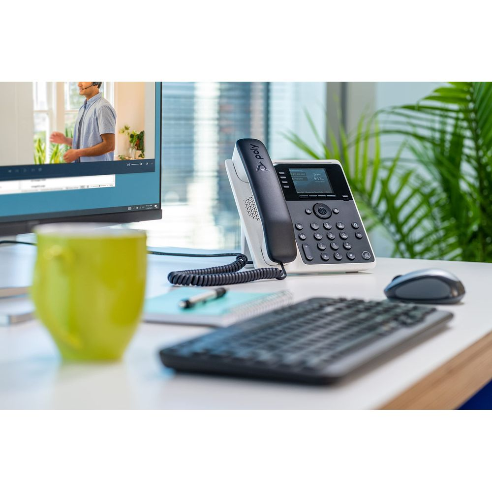 Scrivania con telefono, tastiera, mouse, tazza e monitor che mostra una videochiamata.