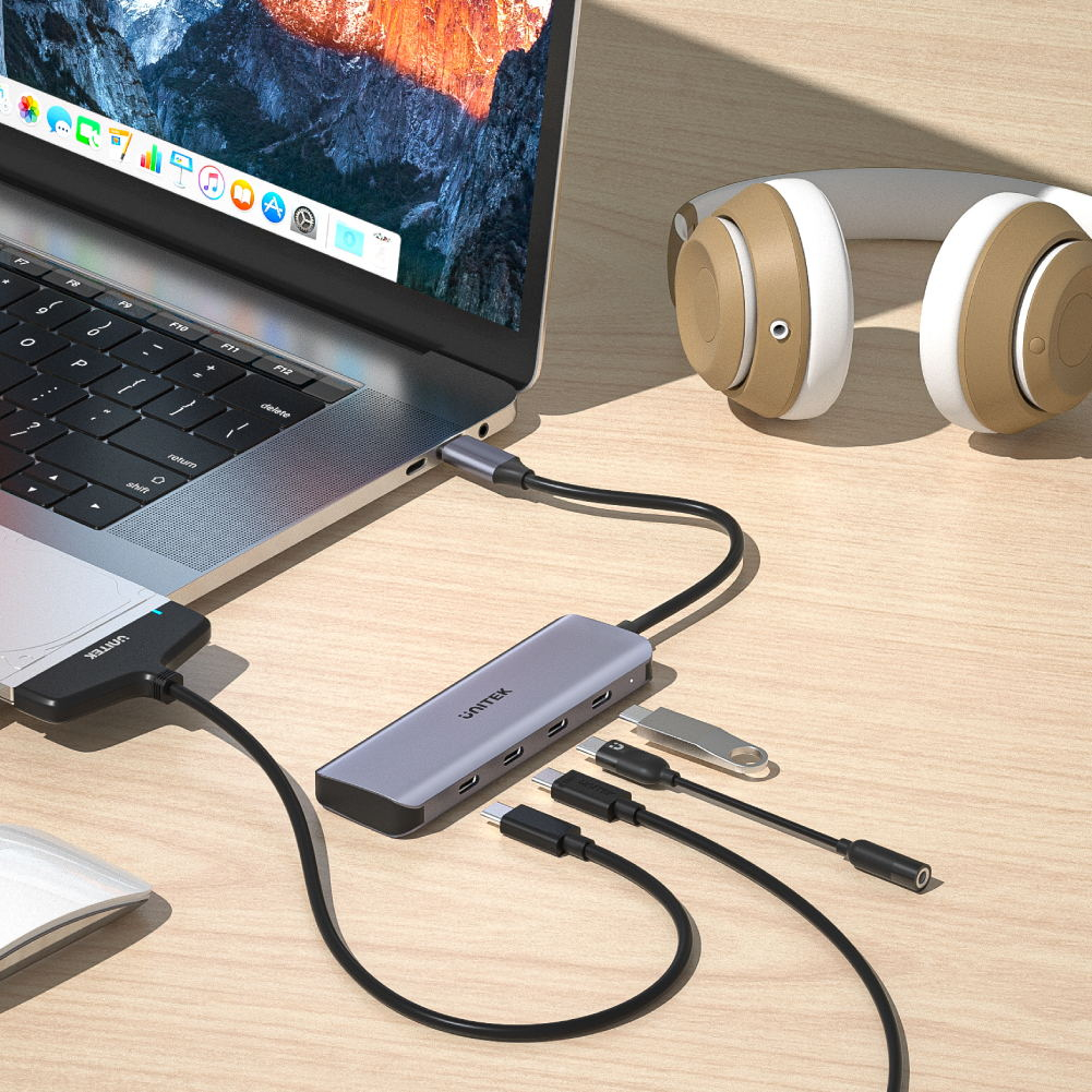 Laptop an USB-C-Hub angeschlossen, daneben Kopfhörer und Maus auf Holztisch.