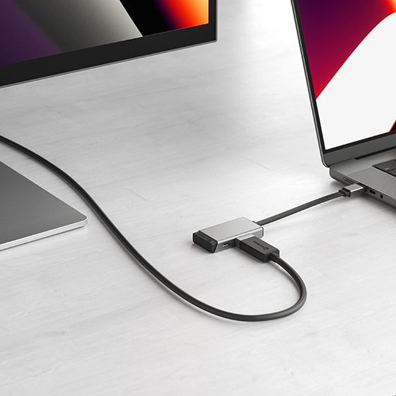 Un hub USB-C argentato si collega a un laptop, con cavi che si estendono a un monitor.