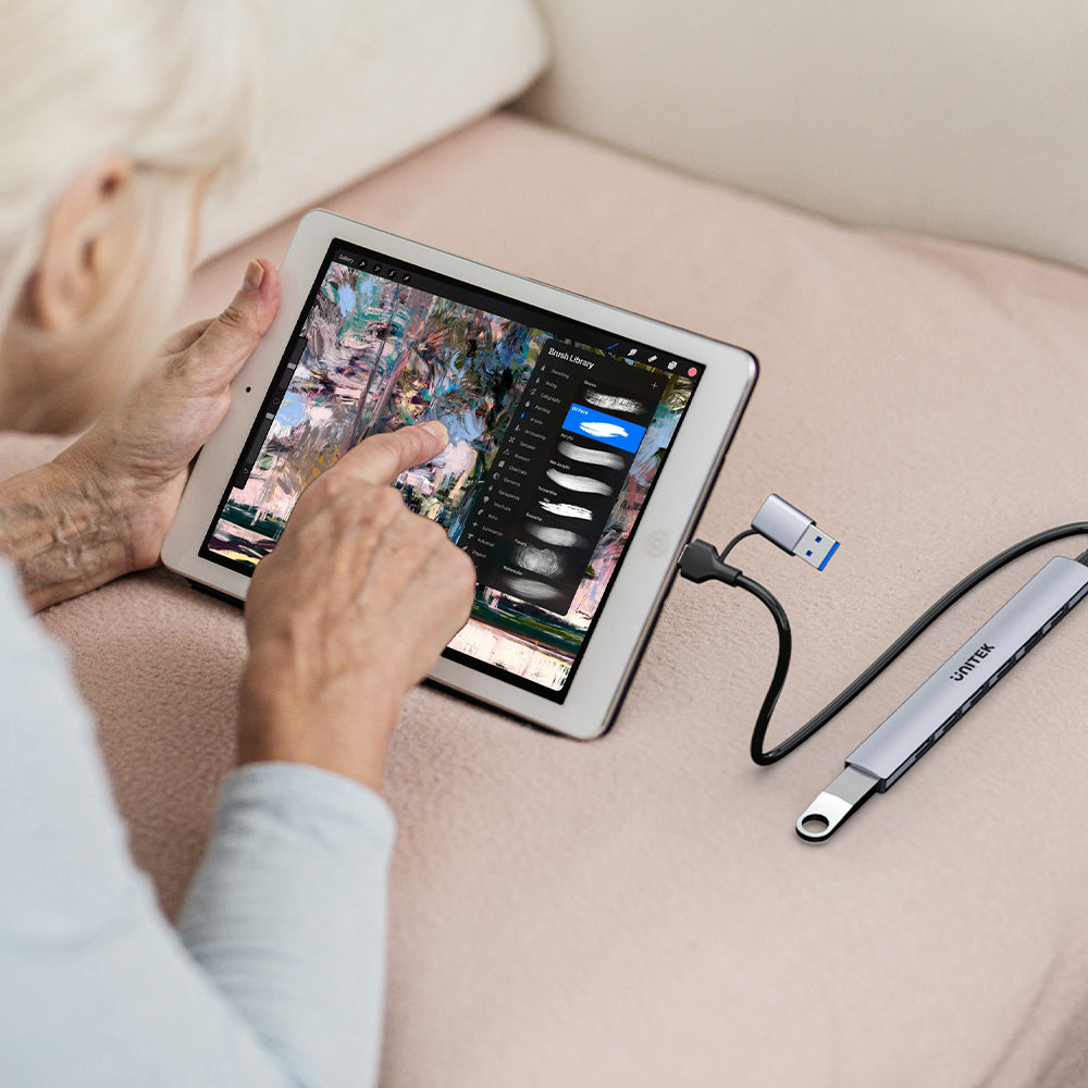 Persona anziana usa tablet con app di pittura digitale e hub USB collegato.