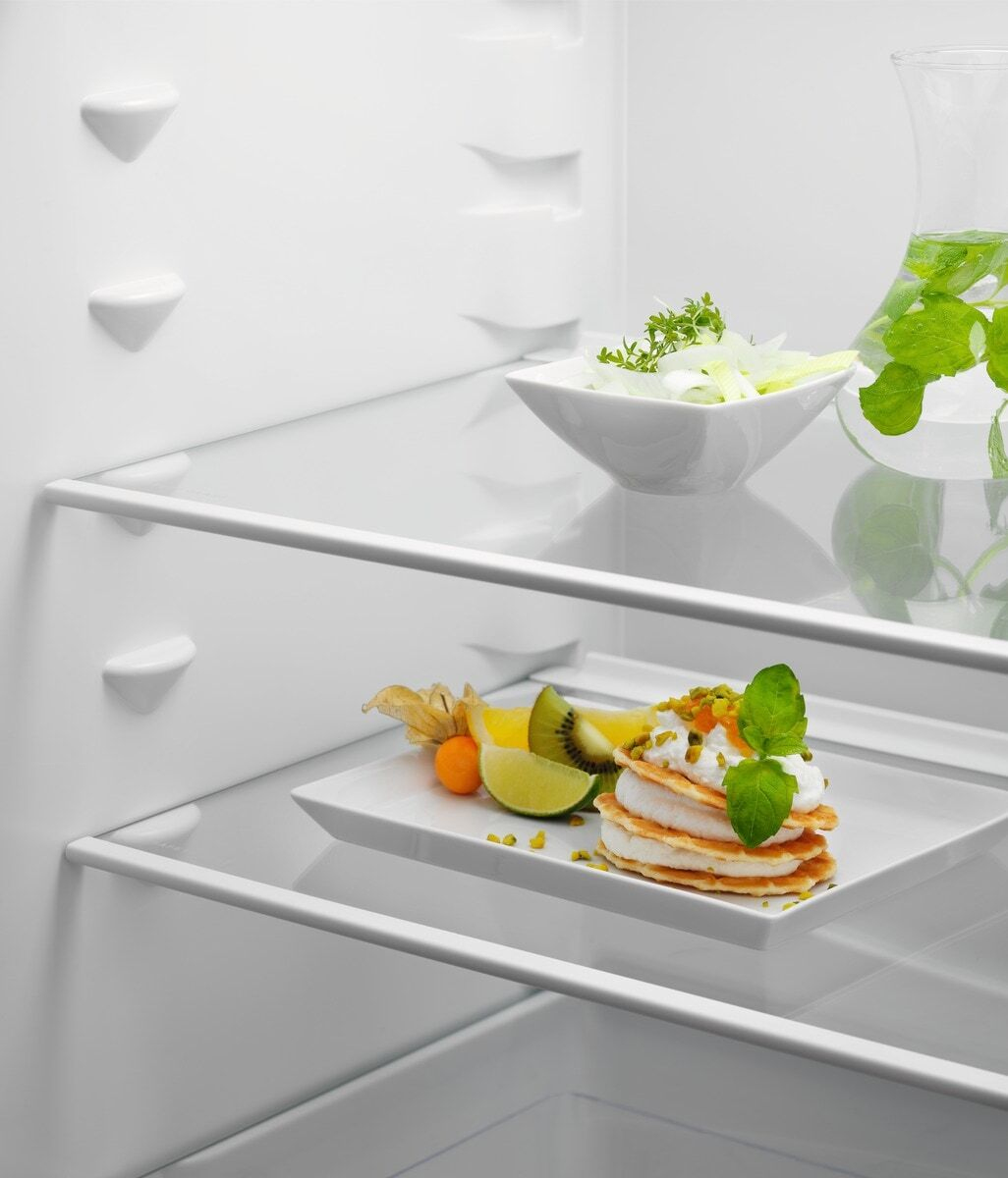 Una pila di pancake con panna e pistacchi, serviti con kiwi, lime e physalis su un piatto in un frigorifero.