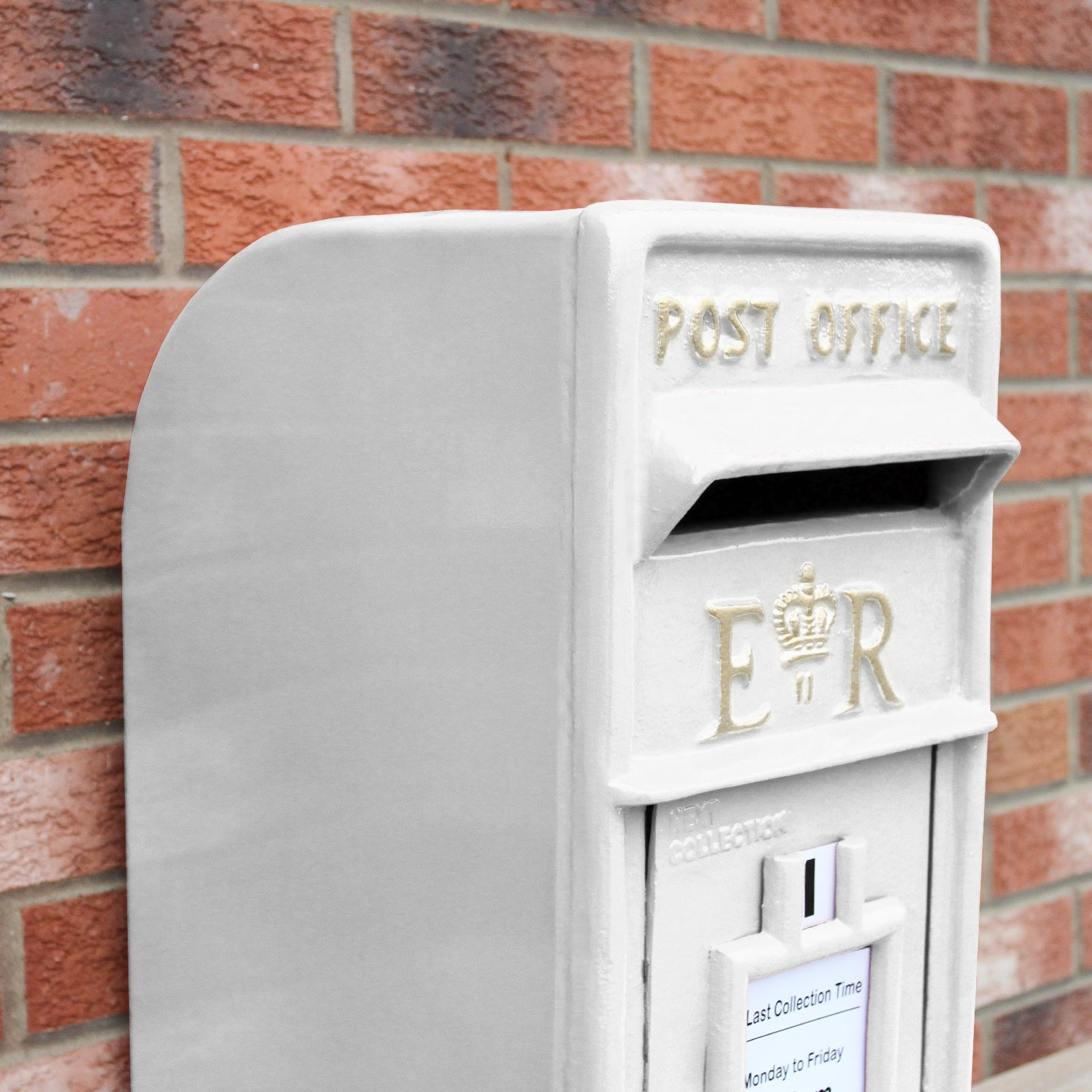 Un buzón blanco con letras doradas 'POST OFFICE' y 'ER' contra una pared de ladrillos.