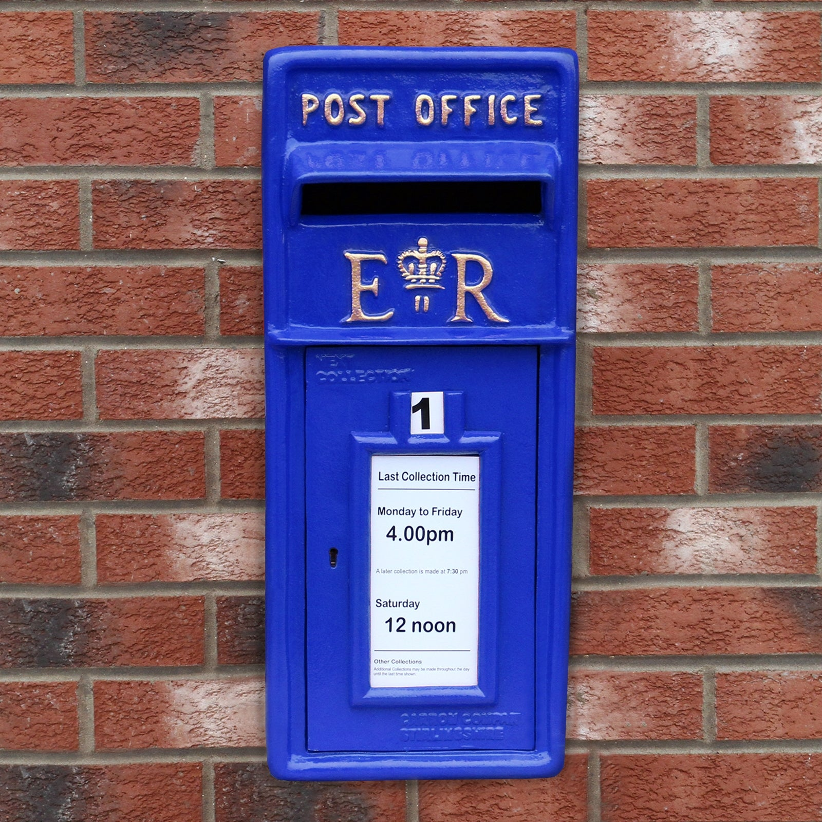 Buzón azul de correos con E.R. y corona en pared de ladrillos.