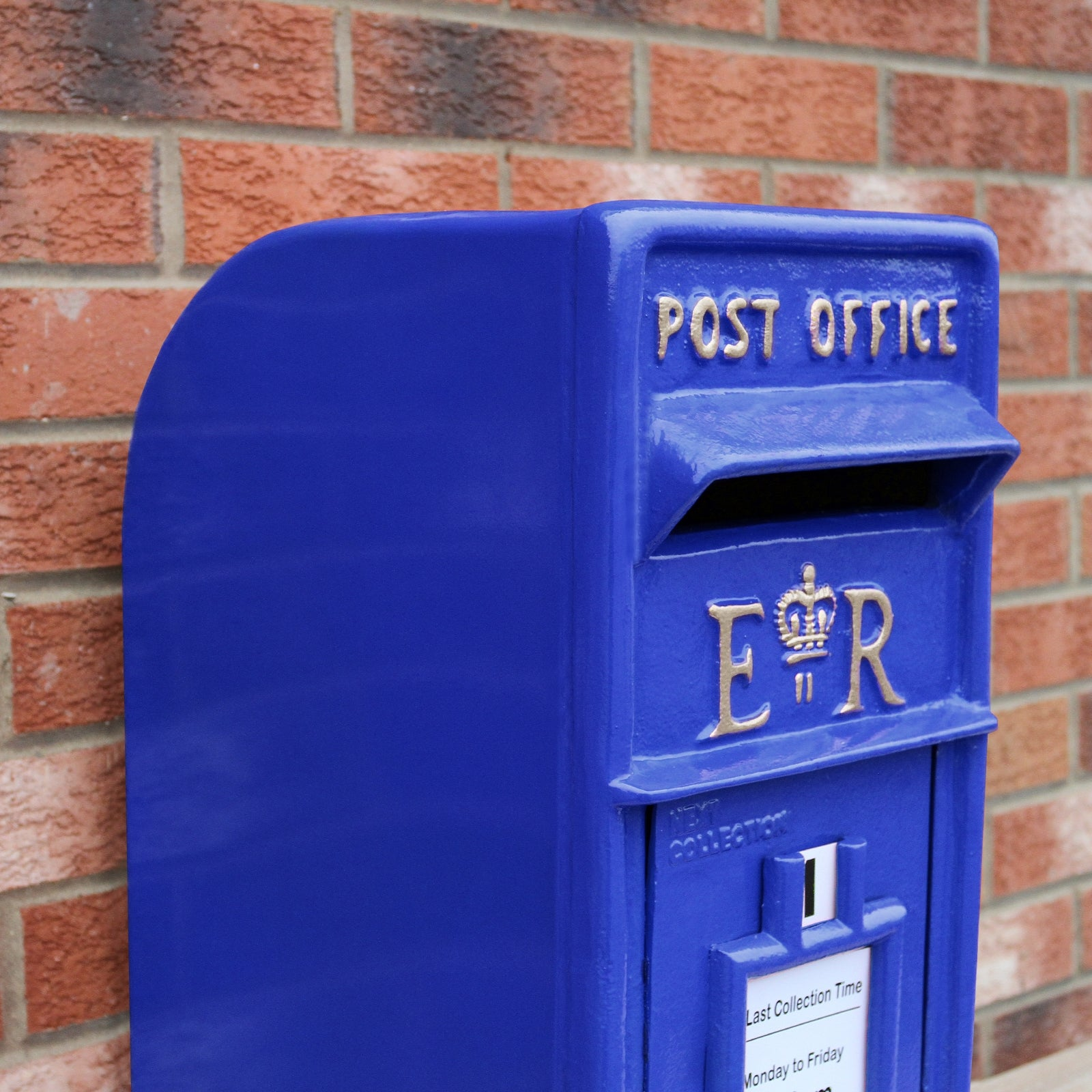 Un buzón azul con letras doradas 'POST OFFICE' contra una pared de ladrillos.