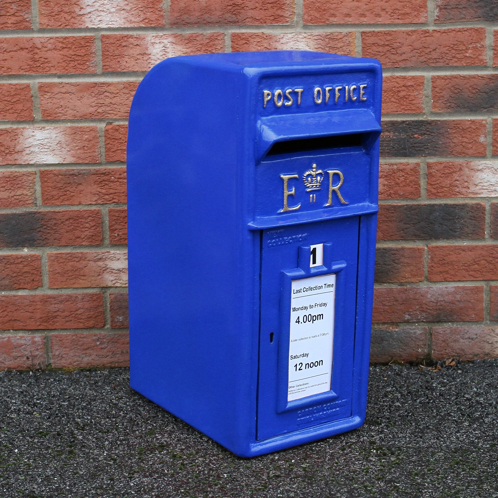 Un buzón azul con "POST OFFICE" y "ER", frente a una pared de ladrillos.