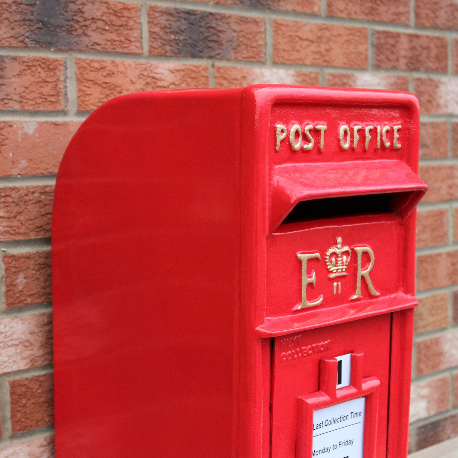 Un buzón rojo con "POST OFFICE" y "ER" en dorado, contra una pared de ladrillos.