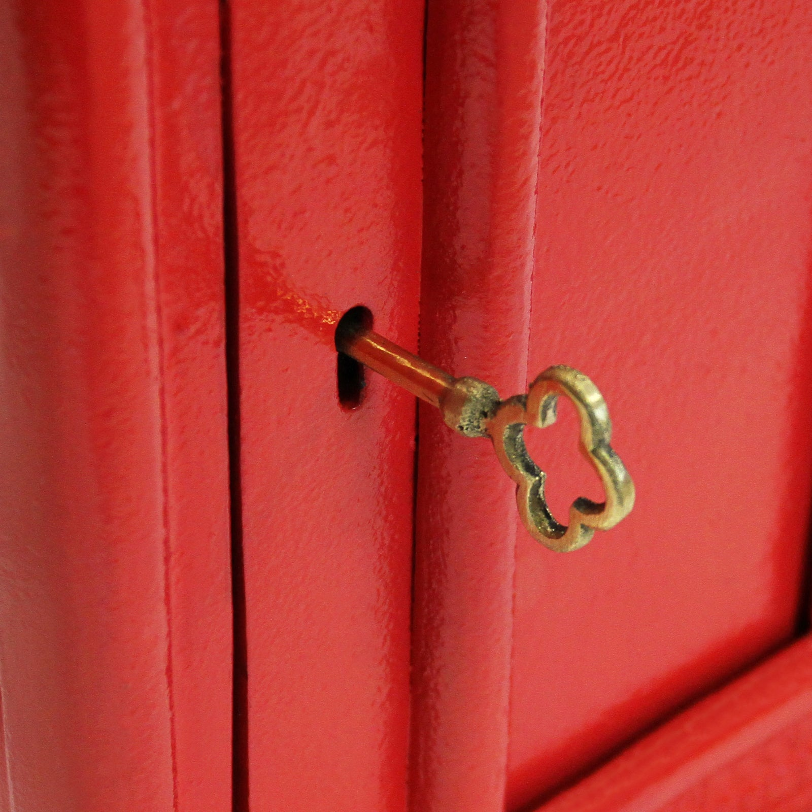 Una llave de latón con cabeza decorativa insertada en una cerradura sobre superficie roja.