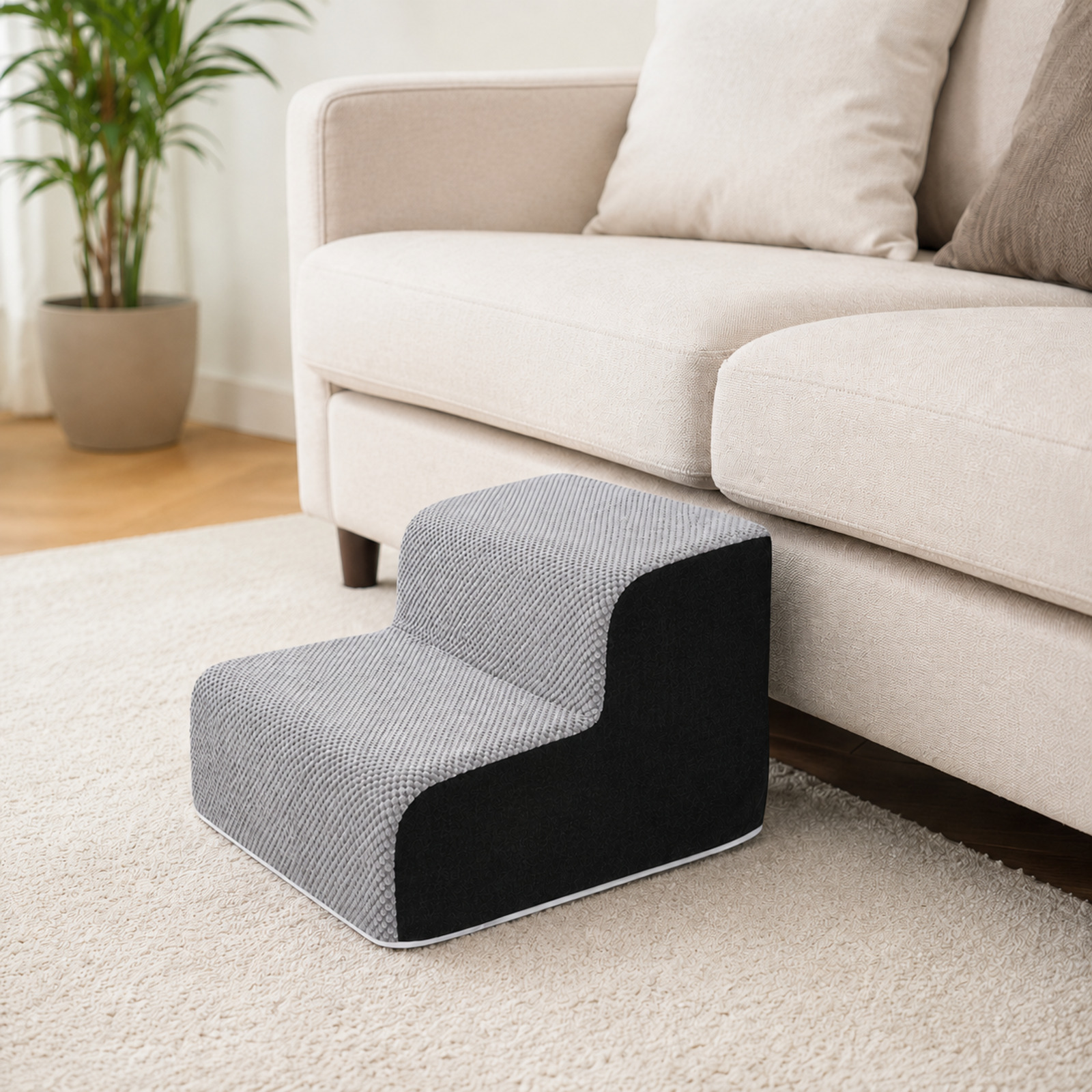 Una escalera para mascotas gris de dos peldaños junto a un sofá beige.