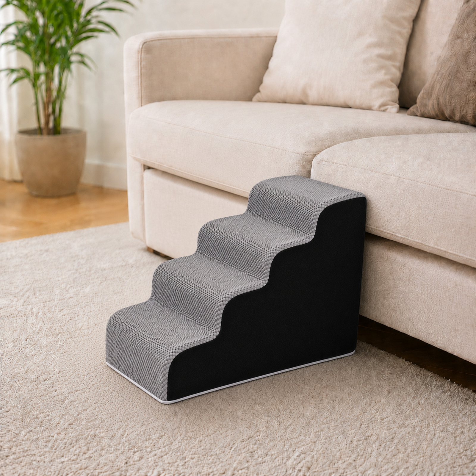 Escaleras grises de tres peldaños para mascotas con laterales negros sobre alfombra crema junto a sofá beige.