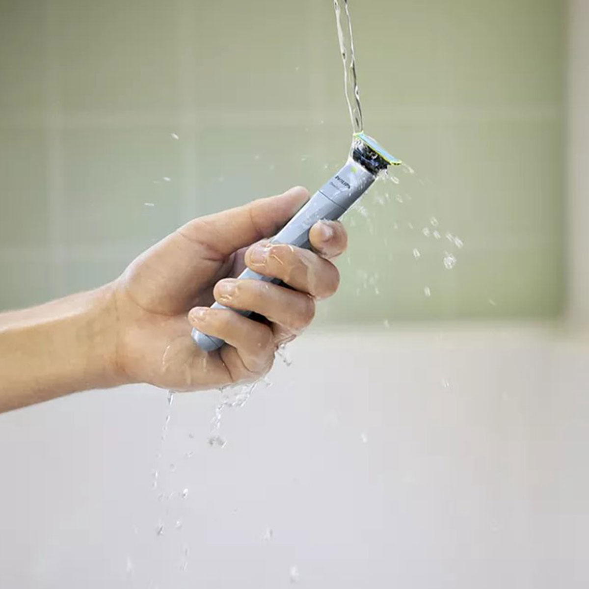 Una mano sostiene una recortadora plateada bajo agua corriente.