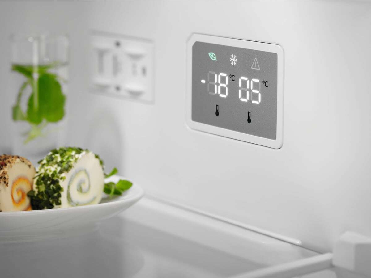 Una pantalla de refrigerador muestra -18°C y 5°C, con queso enrollado al lado.
