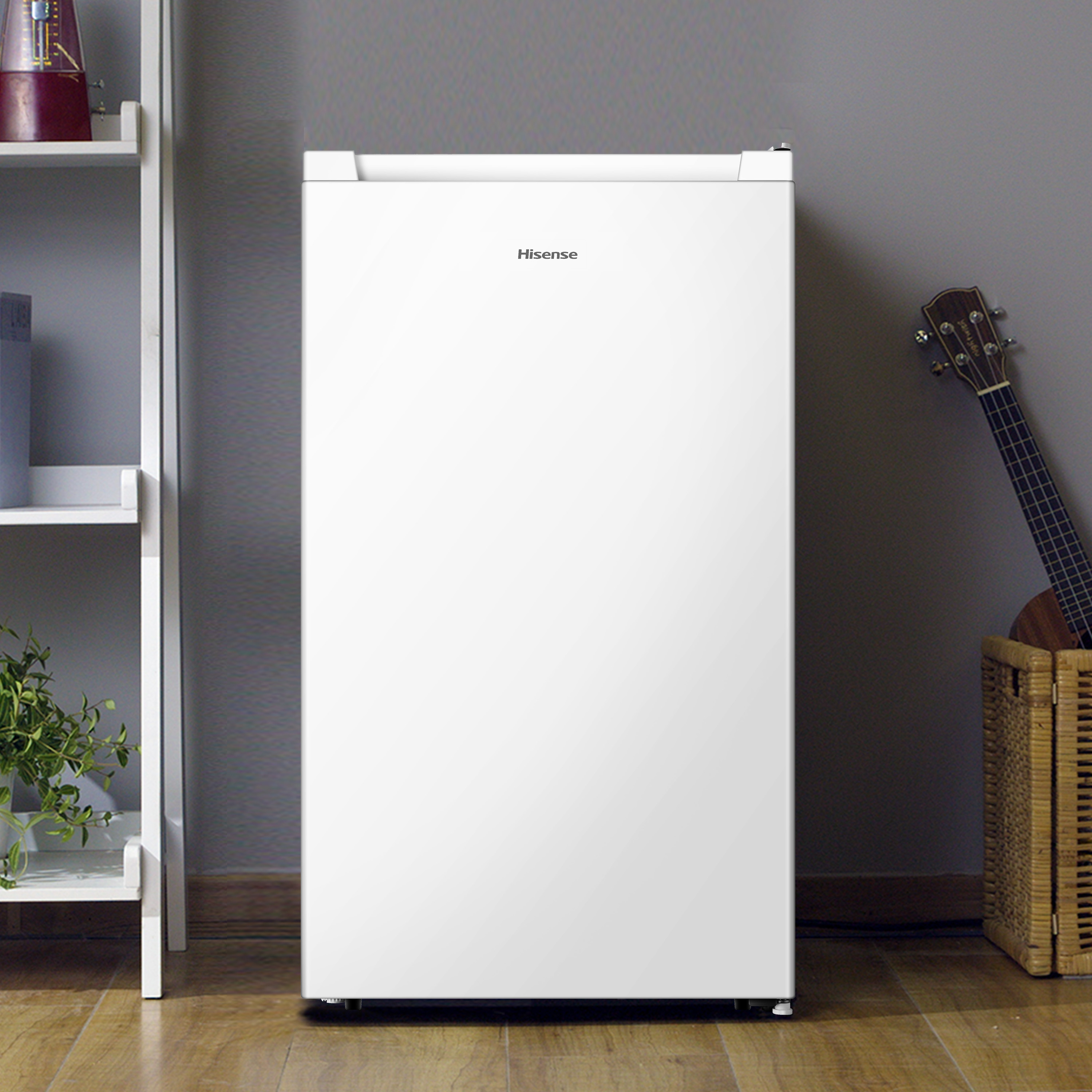 Un réfrigérateur Hisense blanc se trouve sur un plancher en bois à côté d'une étagère avec des plantes.