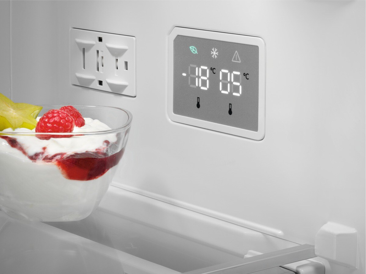Un vaso de yogur con bayas y carambola está en un refrigerador junto a un panel de control.