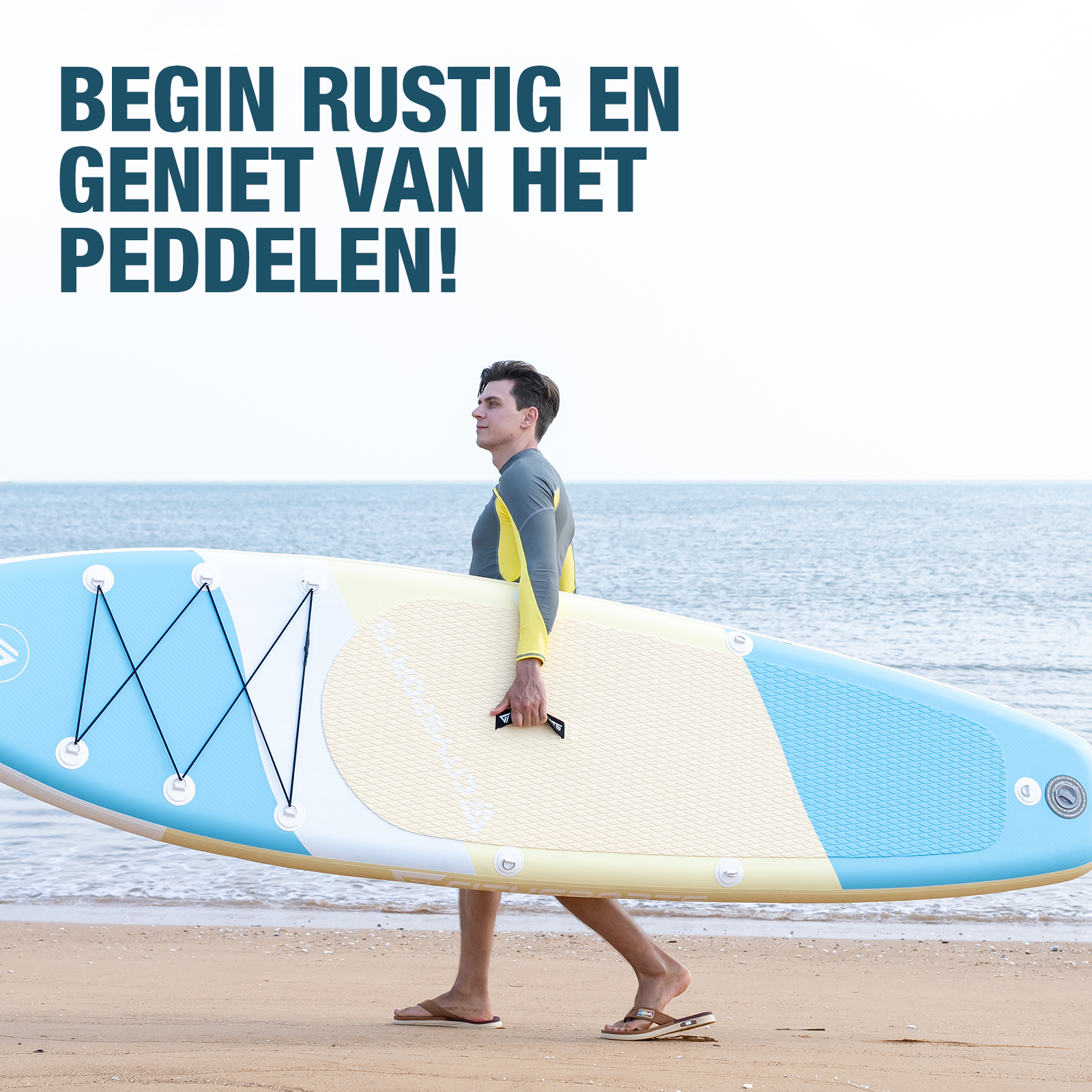 Een man in een wetsuit draagt een SUP board op het strand.