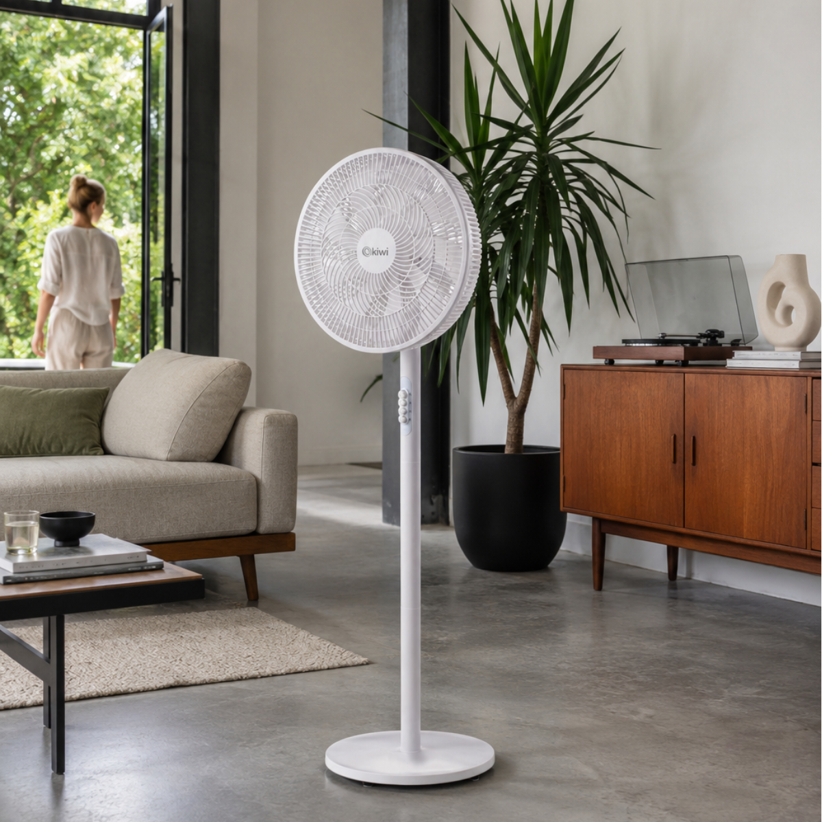 Un ventilatore da terra bianco è in un soggiorno accanto a un divano e una pianta.