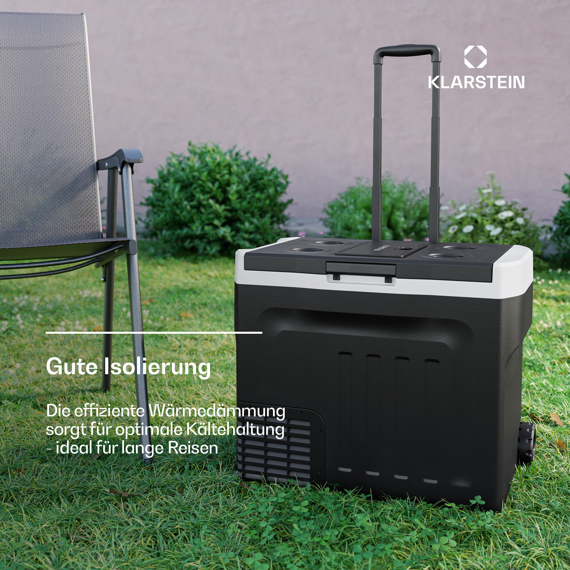 Ein schwarzer Kühlbox auf Rollen steht im Gras vor einem Busch.