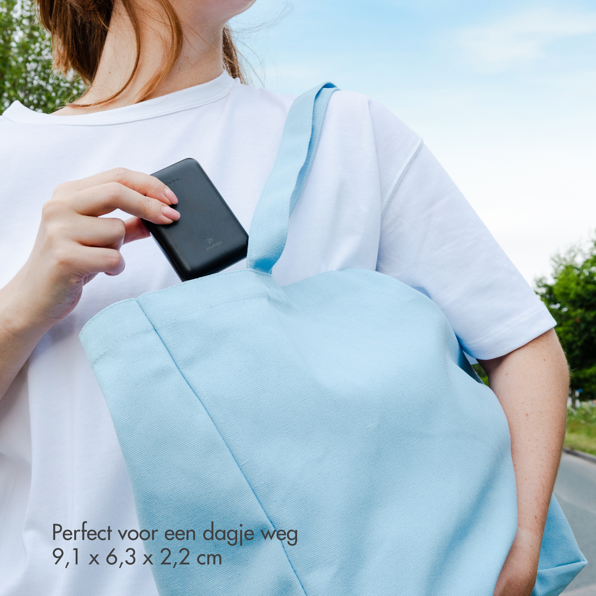 Une femme met une batterie externe noire dans un sac bleu clair. Ciel en arrière-plan.