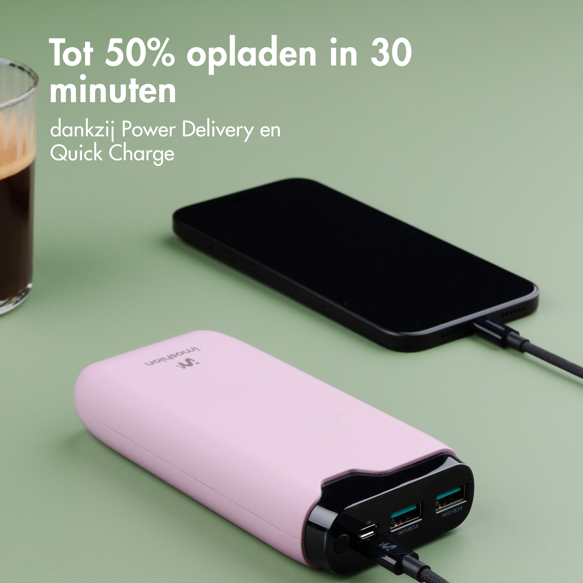 Une power bank rose charge un smartphone noir, avec une tasse de café à proximité.