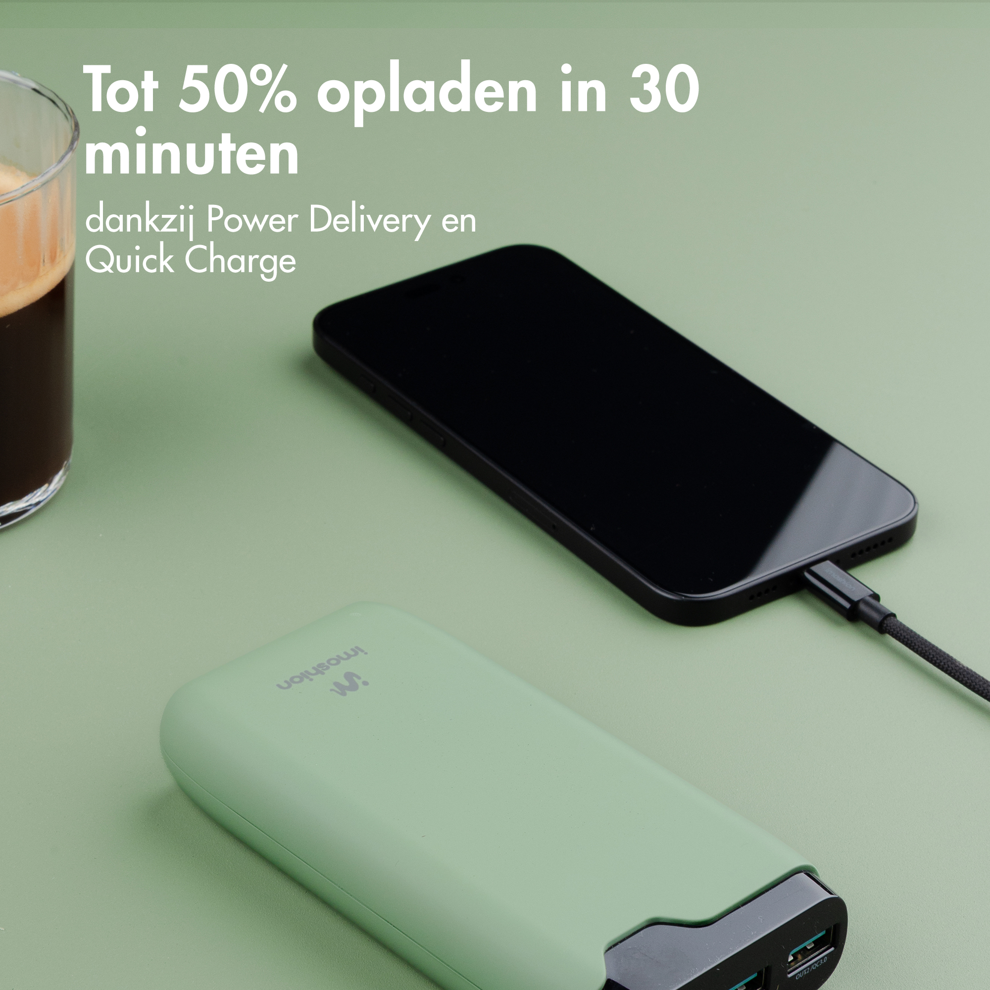 Une batterie externe verte charge un téléphone noir. Café à côté.