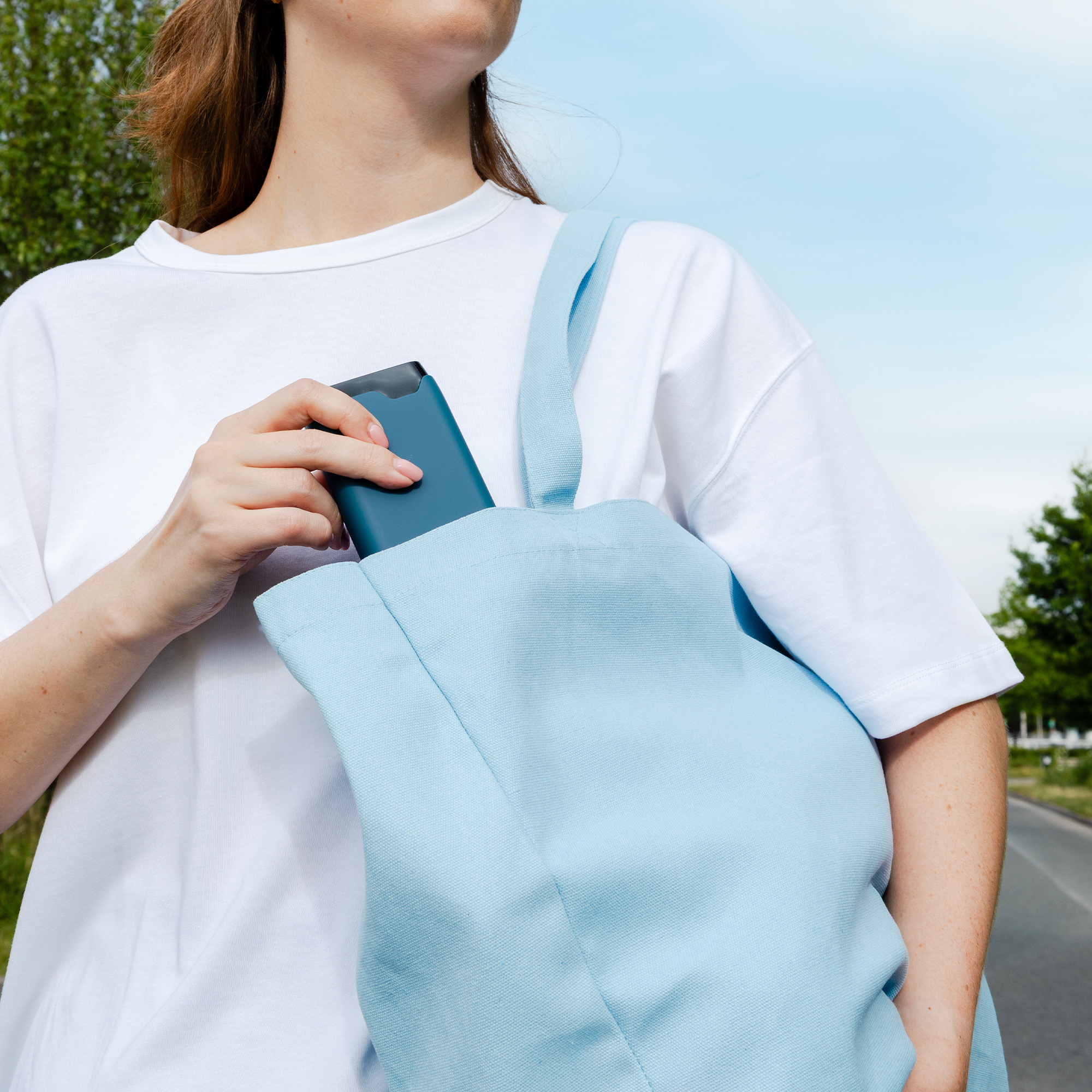 Eine Person in Weiß legt ein blaues Handy in eine hellblaue Tasche.