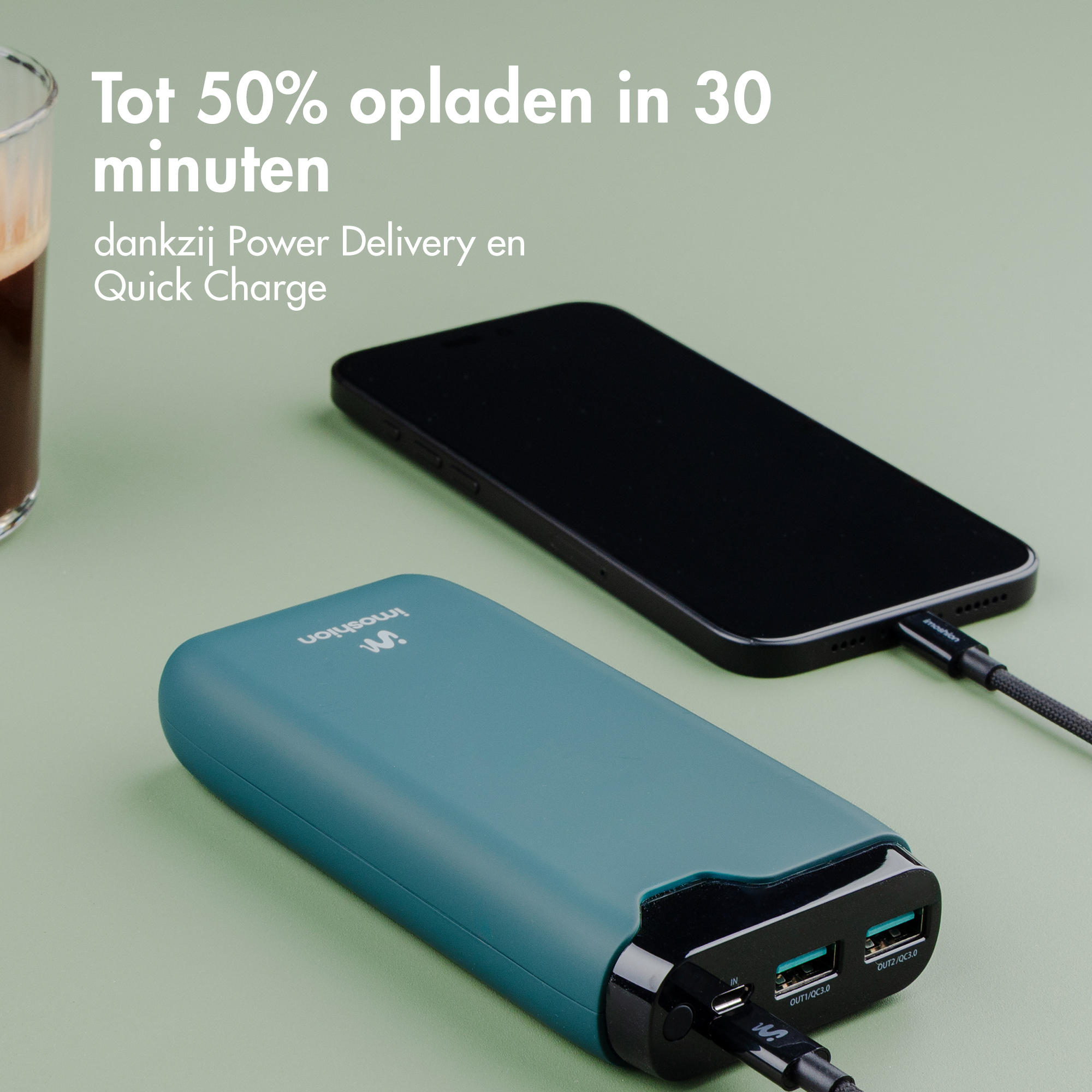 Ein blaugrüner Powerbank lädt ein schwarzes Smartphone. daneben ein Glas Kaffee.