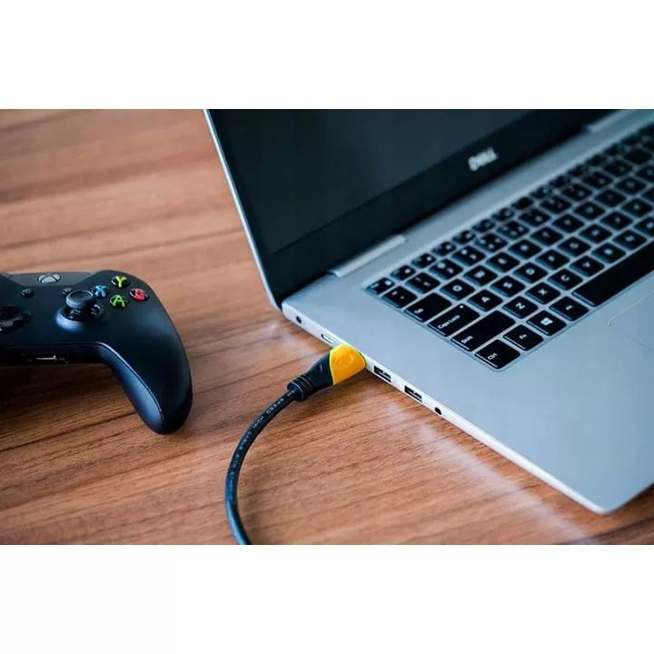 Czarny kontroler leży obok laptopa z podłączonym żółtym kablem.