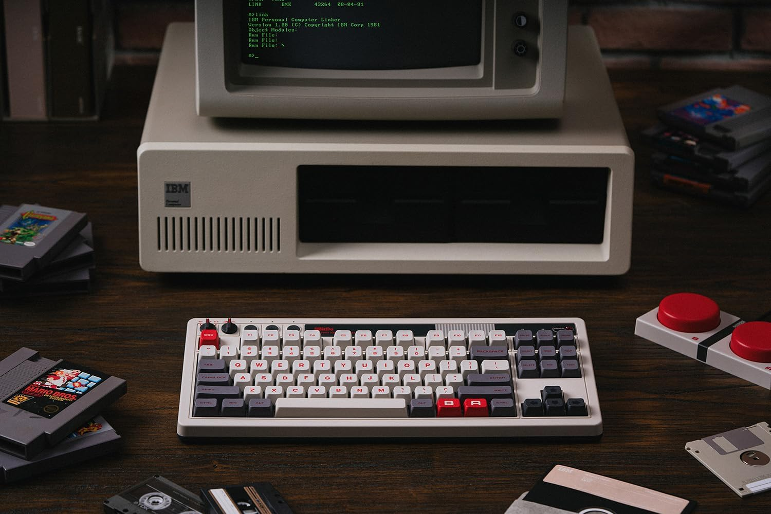 Komputer IBM z klawiaturą, joystickami, kasetami i dyskietkami.