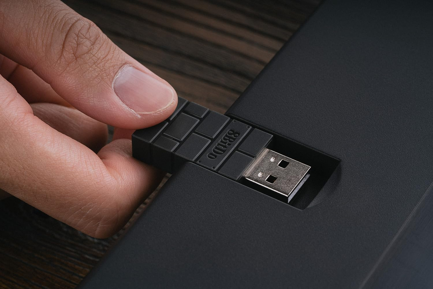 Dłoń wkłada czarny klucz USB do czarnego urządzenia.