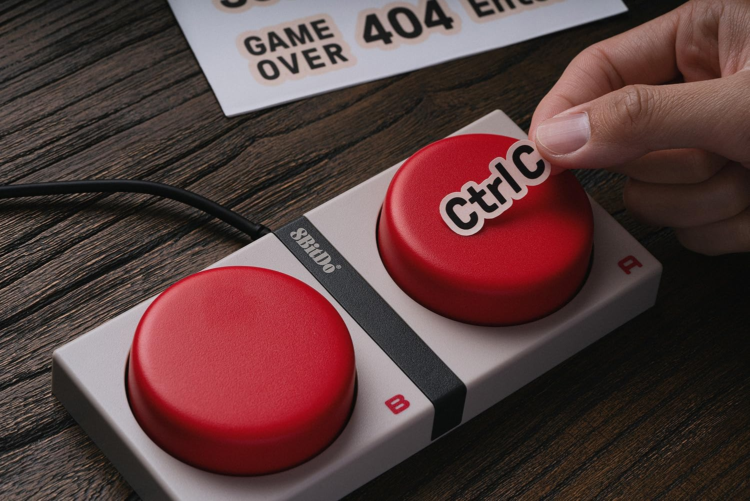Ręka umieszcza naklejkę "Ctrl C" na czerwonym przycisku kontrolera.