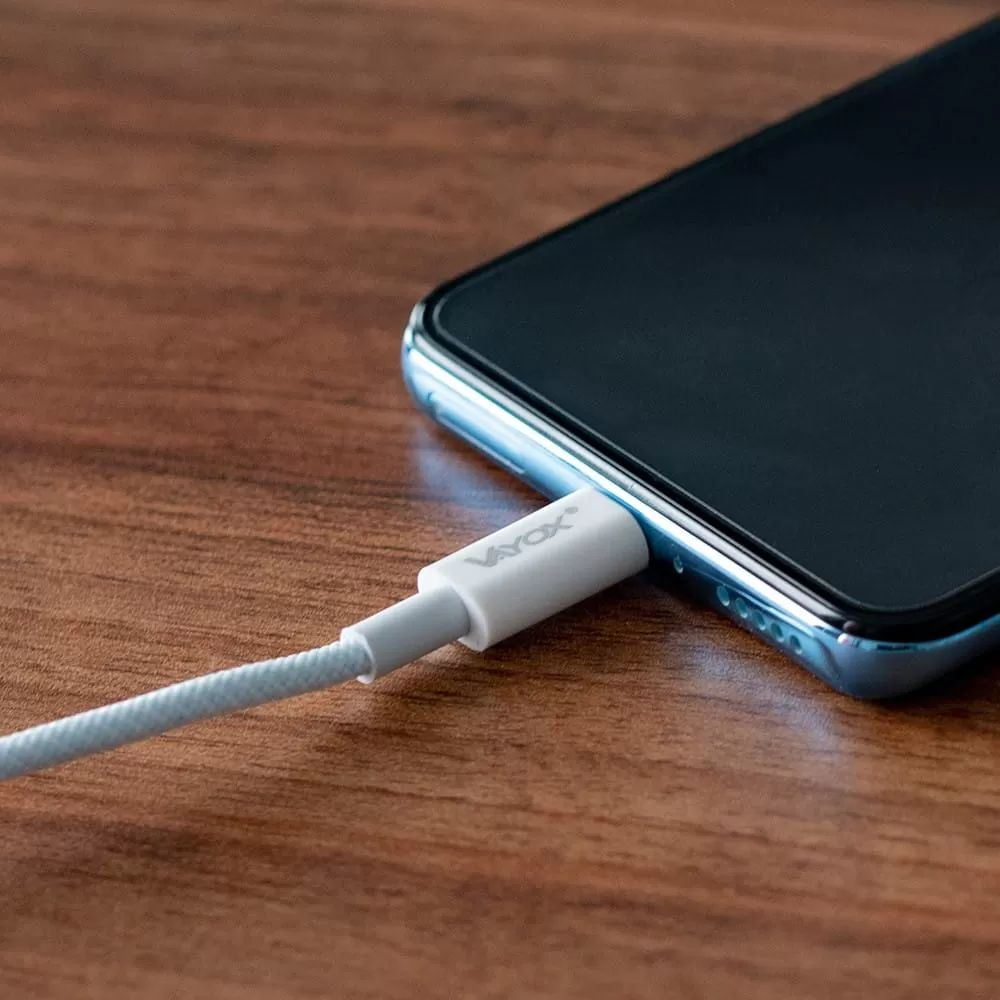 Ein weißes Ladekabel mit der Aufschrift Vayox wird in ein dunkles Smartphone gesteckt.