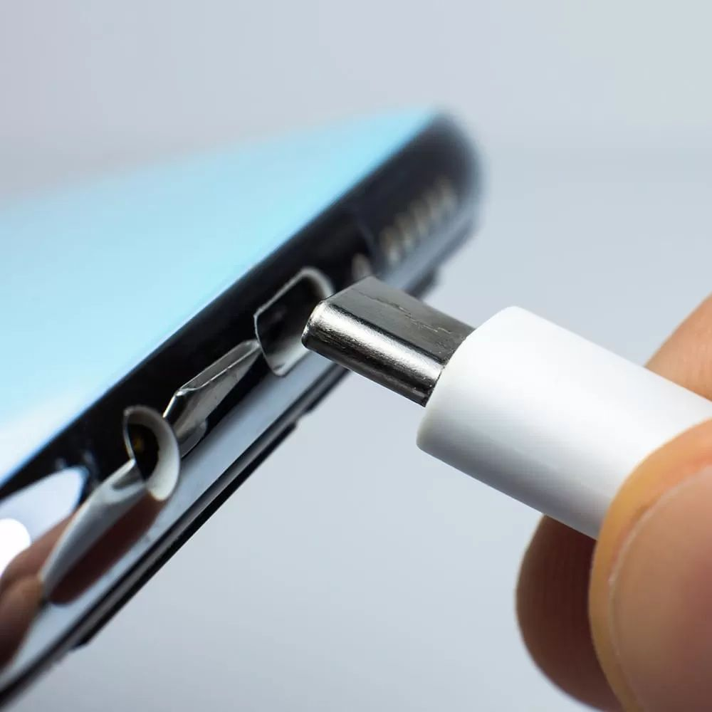 Ein weißes USB-C-Kabel wird in einen blauen Smartphone-Anschluss gesteckt.