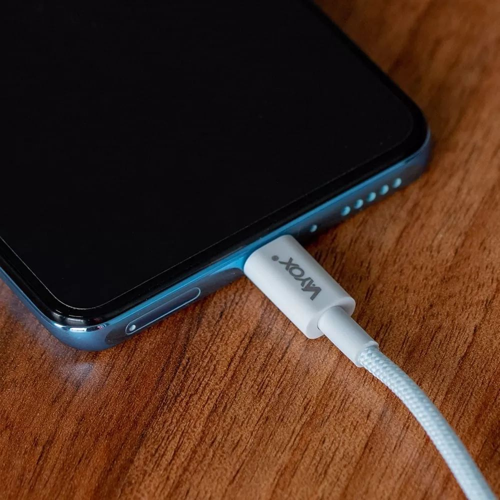 Ein weißes Ladekabel wird in ein Smartphone gesteckt, das auf Holz liegt.