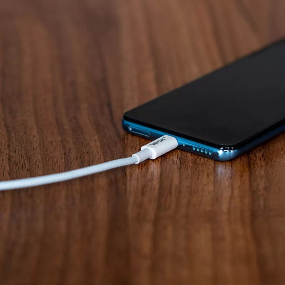 Ein weißes Ladekabel ist an einem blauen Smartphone auf einem Holztisch angeschlossen.