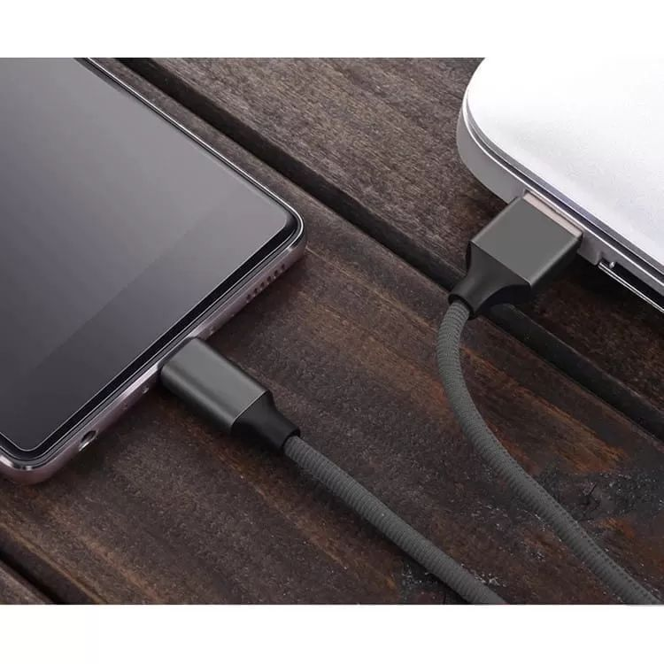 Ein graues USB-Kabel verbindet ein Smartphone mit einem Laptop auf Holztisch.